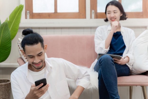 Jeune couple travaillant ensemble à la maison femme assise sur un canapé avec tablette et homme regardant au téléphone