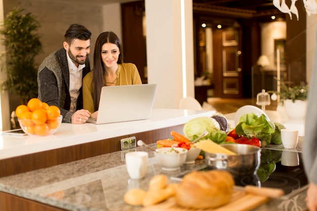 Jeune couple travaillant sur ordinateur portable dans la cuisine