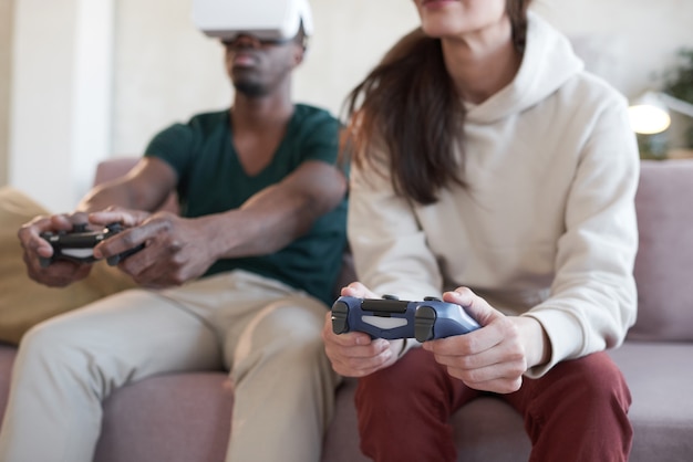 Jeune couple utilisant des manettes de jeu et jouant à un jeu vidéo ensemble sur un canapé dans la chambre