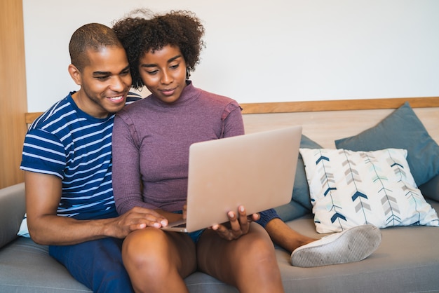 Jeune couple utilisant un ordinateur portable sur un canapé à la maison.