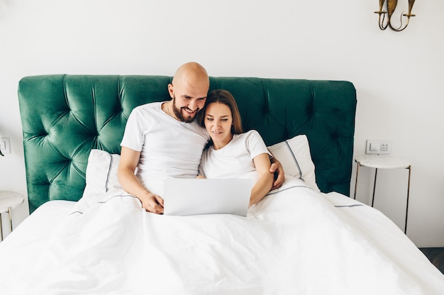 Jeune couple utilisant un ordinateur portable ensemble dans son lit.