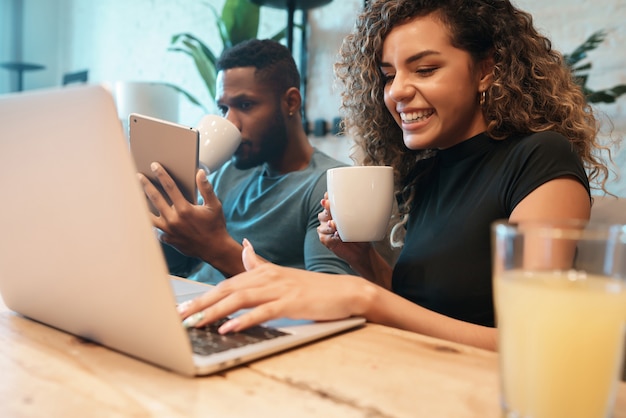 Photo jeune couple utilisant un ordinateur portable et une tablette numérique assis sur une table à la maison.