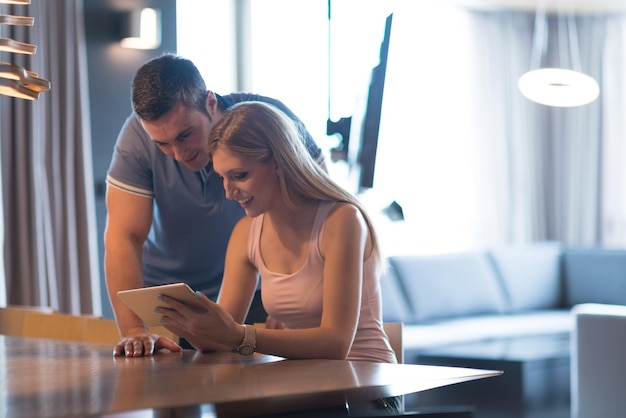 Jeune couple utilisant un ordinateur tablette à la maison de luxe ensemble, regardant l'écran, souriant.