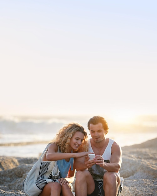 Jeune couple utilisant un smartphone sur la plage au coucher du soleil