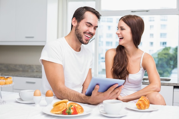 Jeune couple utilisant une tablette au petit déjeuner à la maison dans la cuisine