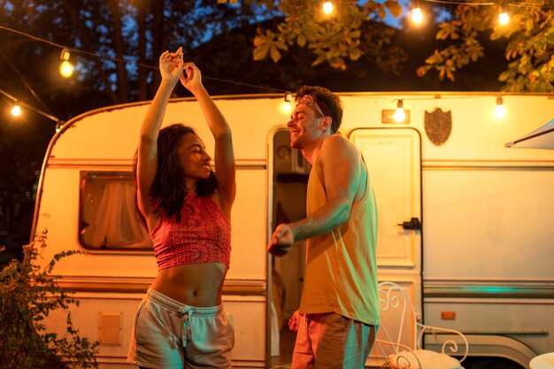 Jeune couple en vacances avec le camping-car. Danser en plein air la nuit. Concept sur les voyages en voiture et le mode de vie en vacances