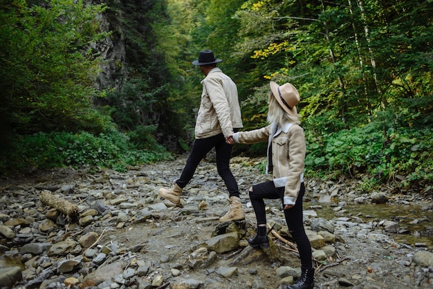 Jeune Couple En Vestes Se Tenant La Main Et Marchant Dans Une Forêt De Pins. L'amour Dans La Nature.