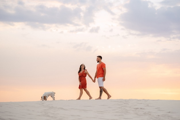 Jeune couple en vêtements orange avec chien dans le sable blanc du désert