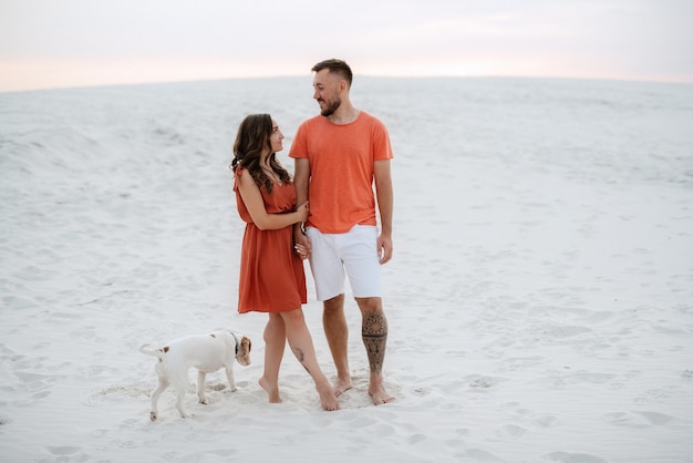 Jeune couple en vêtements orange avec chien dans le sable blanc du désert