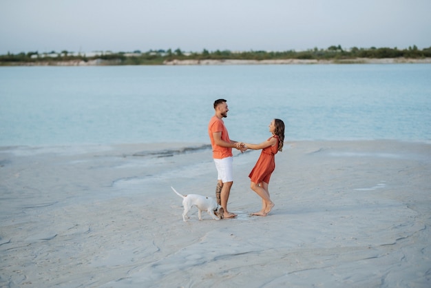 Jeune couple en vêtements orange avec chien sur une plage de sable vide