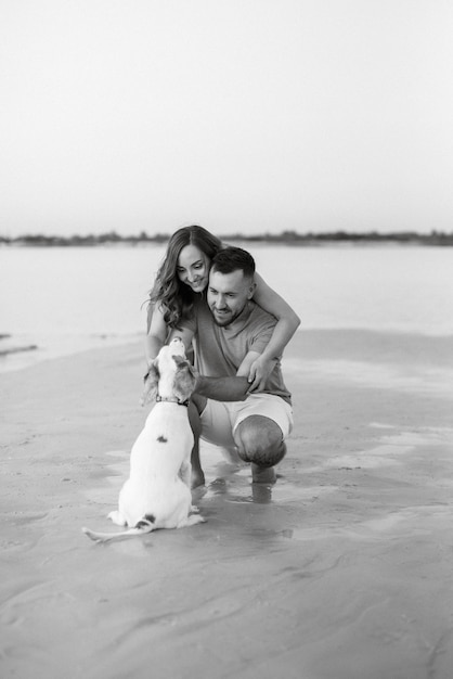 Jeune couple en vêtements orange avec chien sur une plage de sable vide