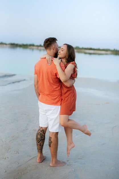 Jeune couple en vêtements orange avec chien sur une plage de sable vide