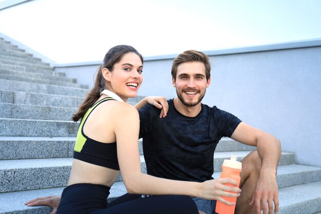 Jeune couple en vêtements de sport assis sur les escaliers après avoir fait de l'exercice à l'extérieur.