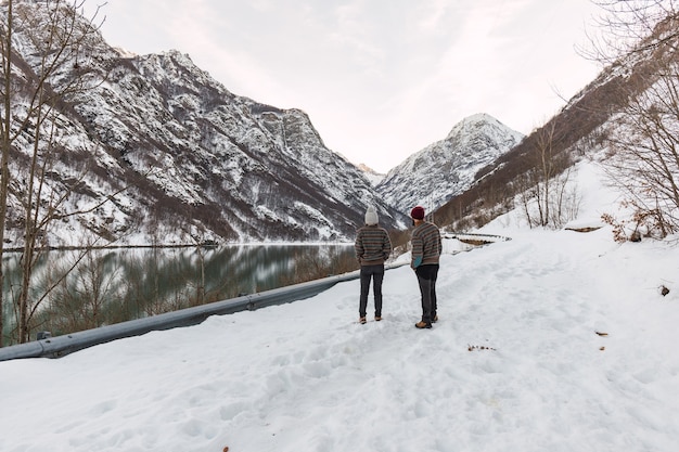 Photo jeune couple vêtu de vêtements d'hiver sur la montagne enneigée à côté d'un lac gelé.