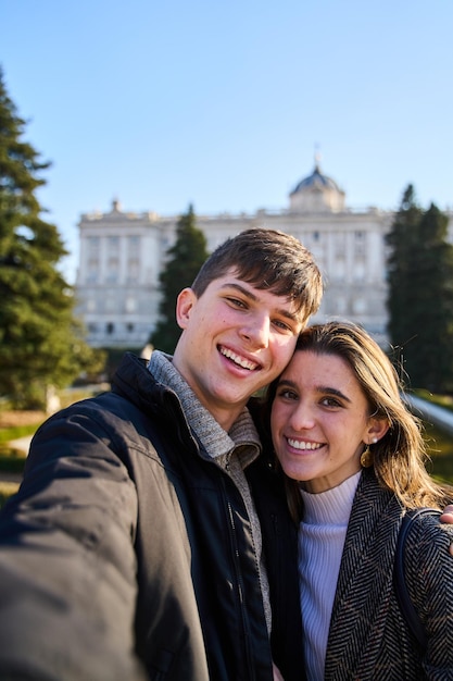 Jeune couple visitant le palais royal de Madrid prenant un selfie avec leurs smartphones