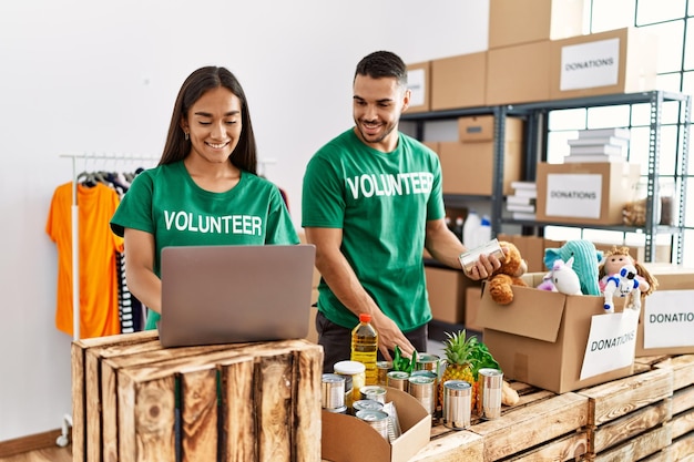 Jeune couple de volontaires latins utilisant un ordinateur portable travaillant au centre caritatif.