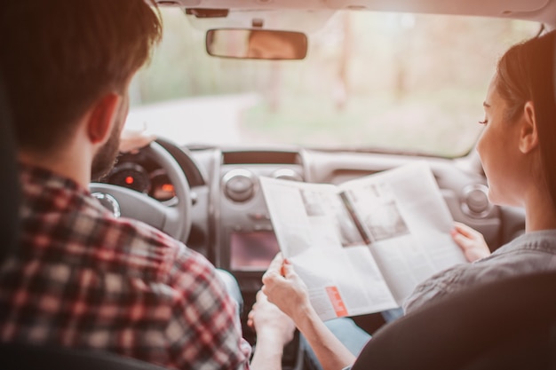 Jeune couple voyage. Ils roulent en voiture. La fille tient la carte et la regarde pendant que le gars conduit. Ils suivent la route.