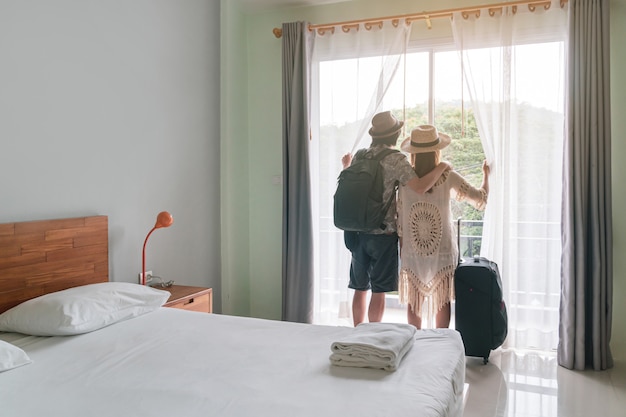 Jeune couple voyageur avec bagages en regardant la vue dans la chambre d'hôtel en vacances d'été