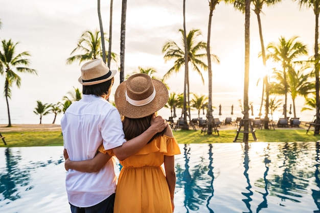 Jeune couple voyageur se détendre et profiter du coucher du soleil au bord d'une piscine tropicale