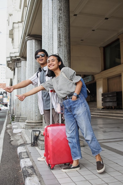 Jeune couple de voyageurs de touristes asiatiques heureux hélant un taxi s'arrêtant avec un geste de la main