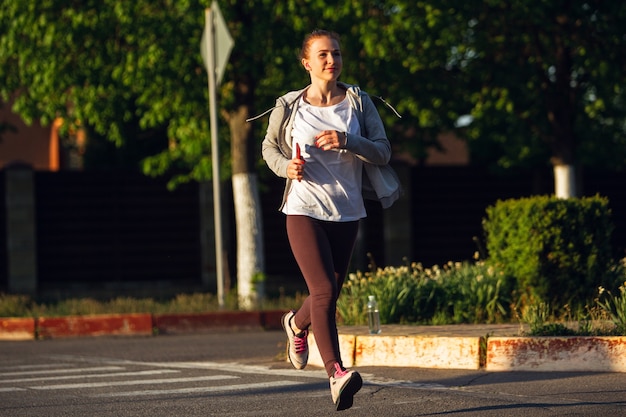 Jeune coureuse, athlète fait du jogging dans la rue de la ville au soleil.