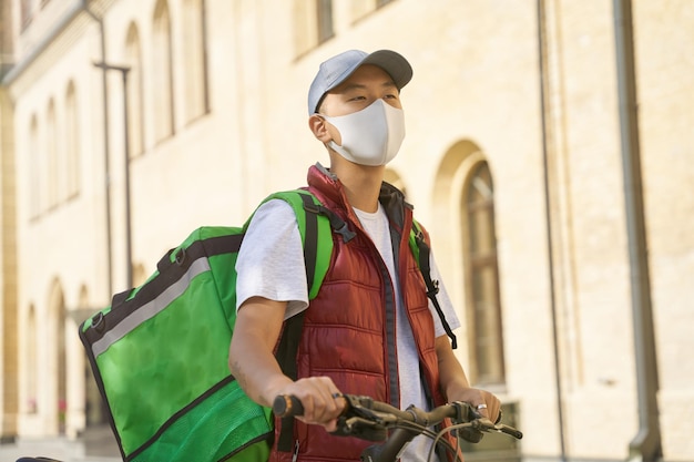 Jeune coursier asiatique avec sac thermo portant une protection faciale