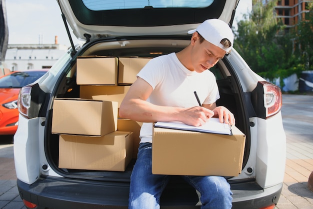 Jeune coursier masculin avec des colis près de la voiture de service de livraison