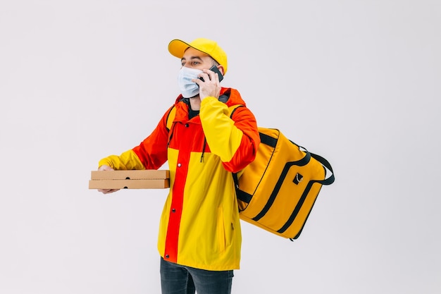 Jeune coursier parlant sur un téléphone portable Courrier masculin avec des boîtes à pizza dans un masque médical avec un sac à dos sur le dos Appel téléphonique