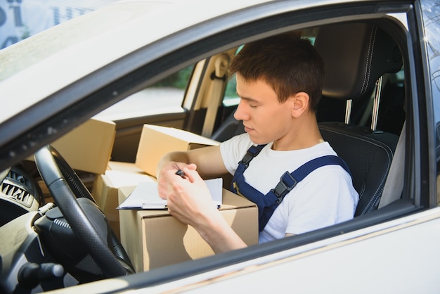 Jeune coursier avec presse-papiers et colis en voiture de livraison