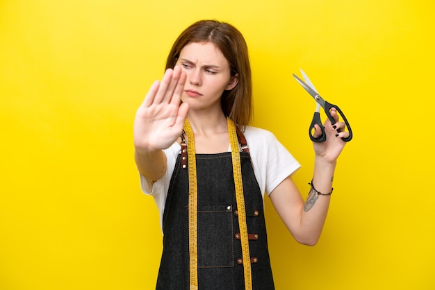 Jeune couturière anglaise femme isolée sur fond jaune faisant un geste d'arrêt et déçue