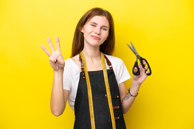 Jeune couturière anglaise femme isolée sur fond jaune heureuse et comptant trois avec les doigts