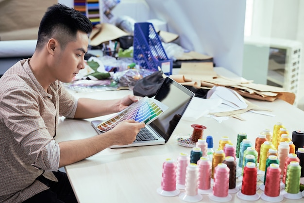 Jeune créateur de mode masculin travaillant à table dans son studio et choisissant les couleurs de la palette