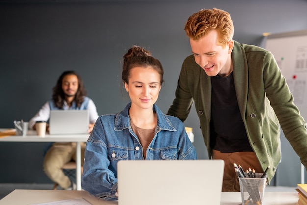 Jeune créatrice confiante et son heureux collègue masculin regardant l'écran de l'ordinateur portable tout en préparant la présentation de la nouvelle application mobile