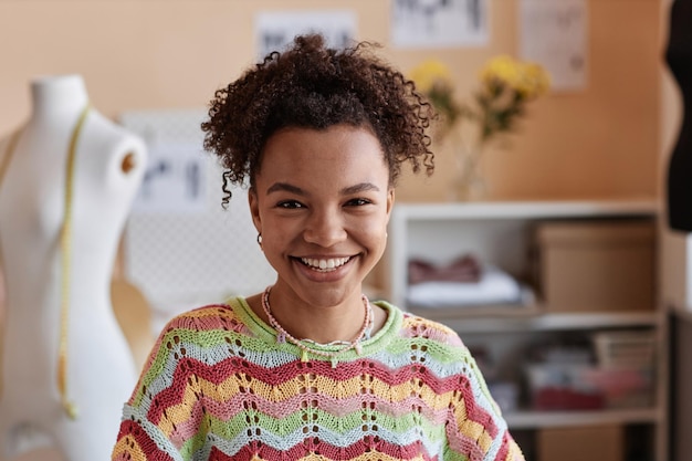 Une jeune créatrice de mode souriante qui regarde la caméra dans son atelier