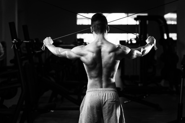 Jeune culturiste de remise en forme musculaire faisant des exercices de poids lourds pour le dos ou les épaules sur la machine dans la salle de gym