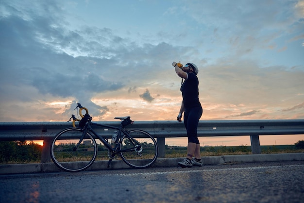 Un jeune cycliste sportif avec un casque et des vêtements confortables se tient au bord de la route avec un vélo et