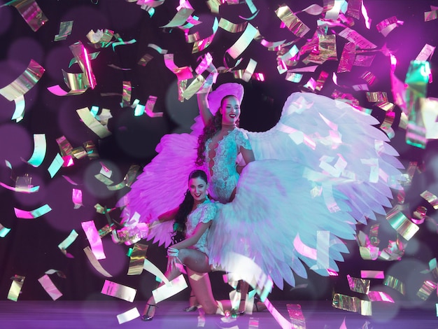 Jeune danseuse avec des ailes d'ange en néon sur fond noir dans des confettis volants