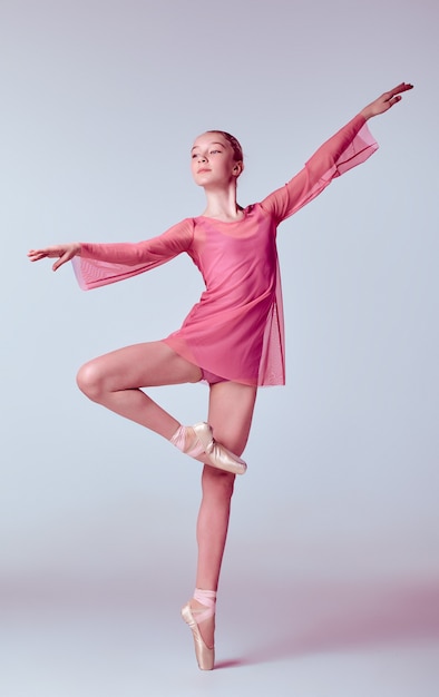 Jeune danseuse ballerine en robe rose montrant ses techniques sur fond lilas