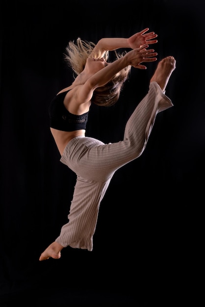 Jeune danseuse en séance photo en studio avec un ballet de fond noir effectuant un saut