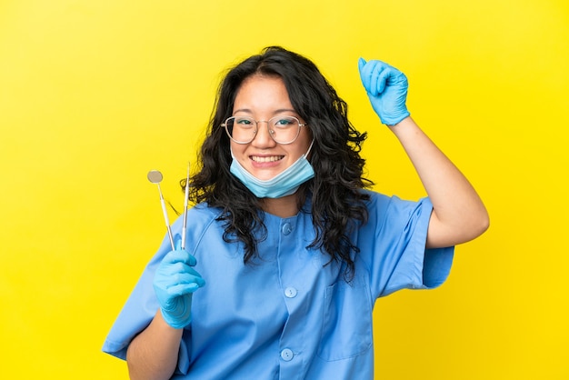Jeune dentiste asiatique tenant des outils sur fond isolé célébrant une victoire