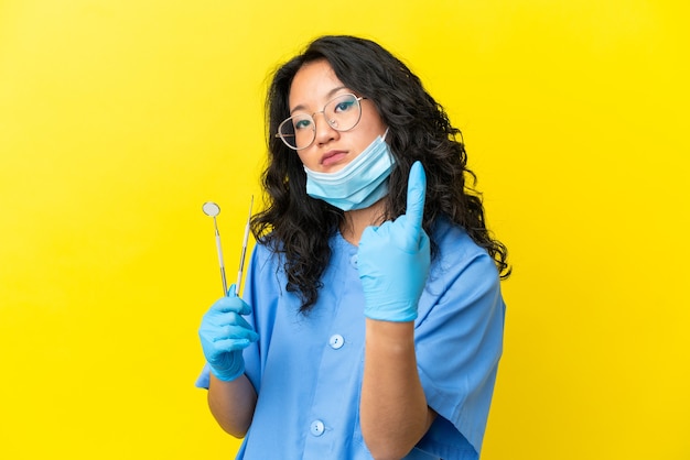 Jeune dentiste asiatique tenant des outils sur fond isolé faisant un geste à venir