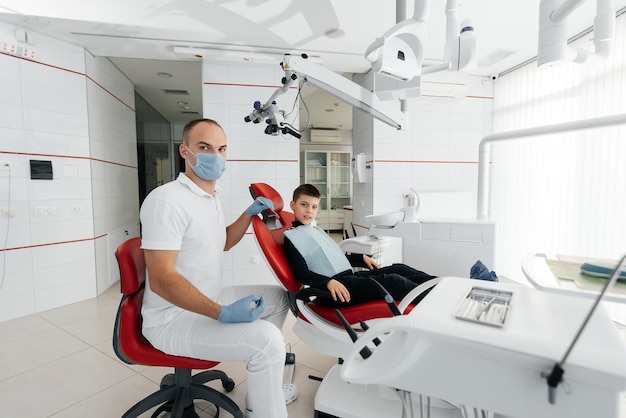 Un jeune dentiste examine et traite les dents d'un garçon de huit ans en dentisterie blanche moderne en gros plan Traitement des prothèses dentaires et blanchiment des dents Dentisterie moderne Prévention