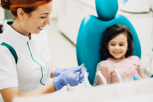 Jeune dentiste pédiatrique prépare le dépôt de la prochaine intervention chirurgicale sur les dents d'un enfant.