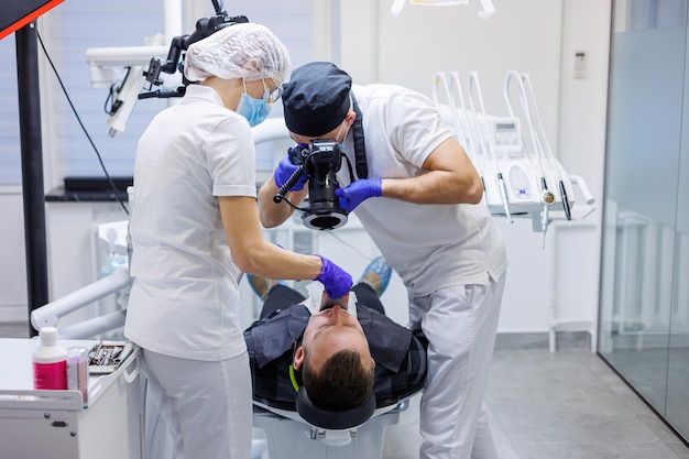 Un jeune dentiste prend une photo des dents du patient L'assistant aide le médecin Cabinet dentaire