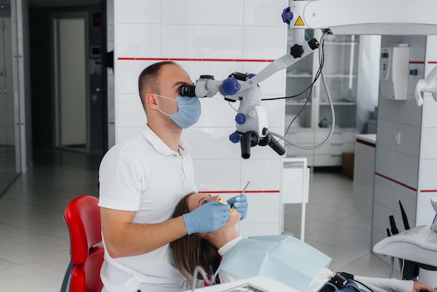 Un jeune dentiste spécialiste examine et traite les dents d'une belle femme en dentisterie blanche moderne à l'aide d'un microscope Traitement des prothèses dentaires et blanchiment des dents