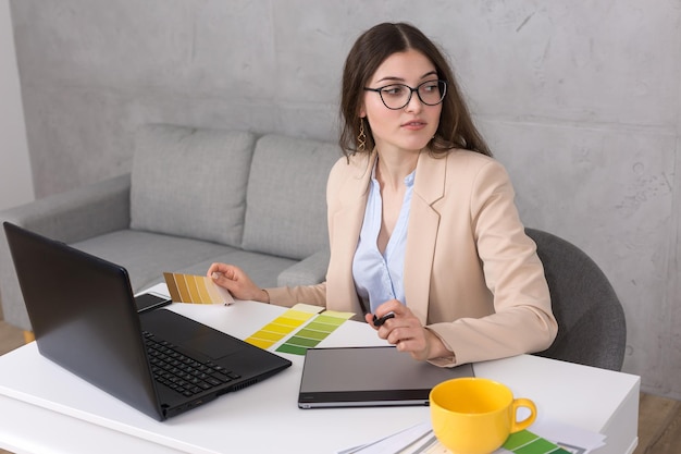 Une jeune designer assise à une table dessine sur une tablette. Effectue des calculs commerciaux sur l'ordinateur.