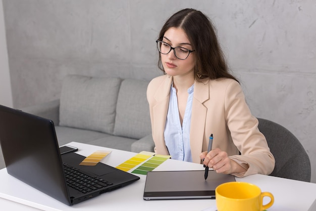 Une jeune designer assise à une table dessine sur une tablette Effectue des calculs commerciaux sur l'ordinateur