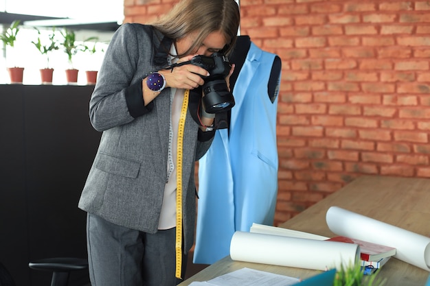 Jeune designer concentrée utilisant un appareil photo numérique tout en se tenant près du bureau dans son bureau de création.