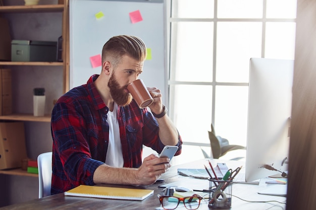 Jeune designer créatif appréciant une boisson chaude dans son bureau