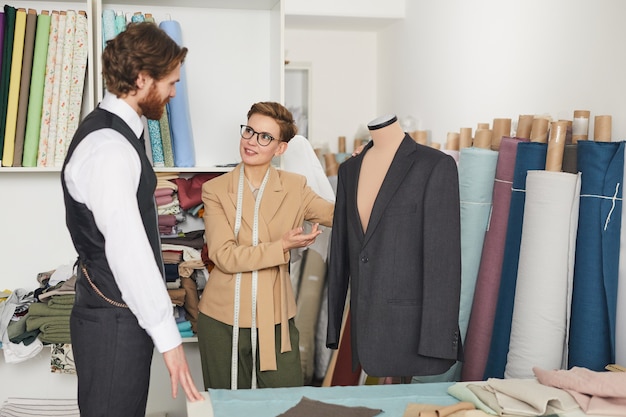 Jeune designer montrant la veste accrochée à un mannequin et parlant à son client dans l'atelier